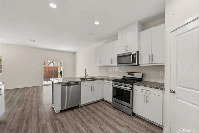 a kitchen with stainless steel appliances granite countertop white cabinets a sink a stove a microwave and a refrigerator