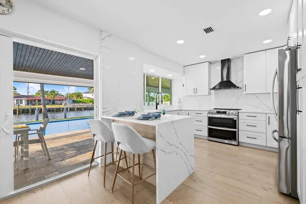 a kitchen with stainless steel appliances granite countertop a sink a stove a refrigerator and white cabinets with wooden floor