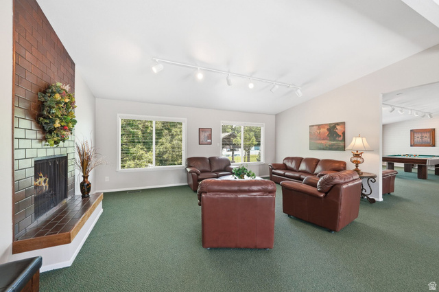 6969 South 855 East Midvale, UT 84047 - Photo 47 of 55 Expansive room featuring a brick fireplace with a wood mantle, green carpeting, multiple windows providing natural illumination, and track lighting