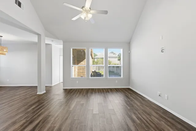 an empty room with wooden floor fan and windows