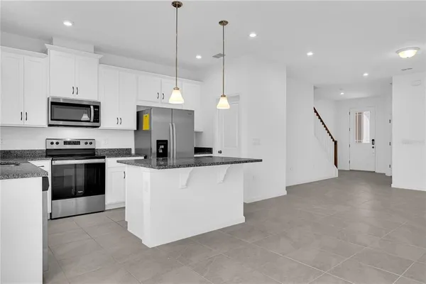 a large kitchen with stainless steel appliances kitchen island granite countertop a stove a sink a microwave a refrigerator and a view of living room