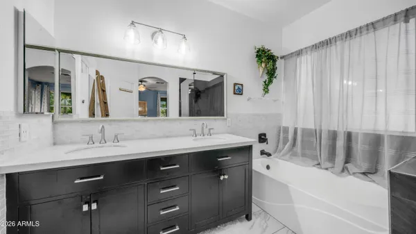 a bathroom with a double vanity sink a large mirror a bathtub and next to a window