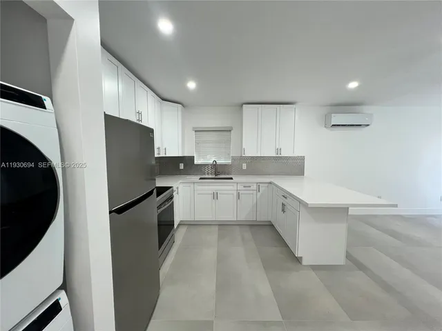 a large white kitchen with a sink a refrigerator and cabinets