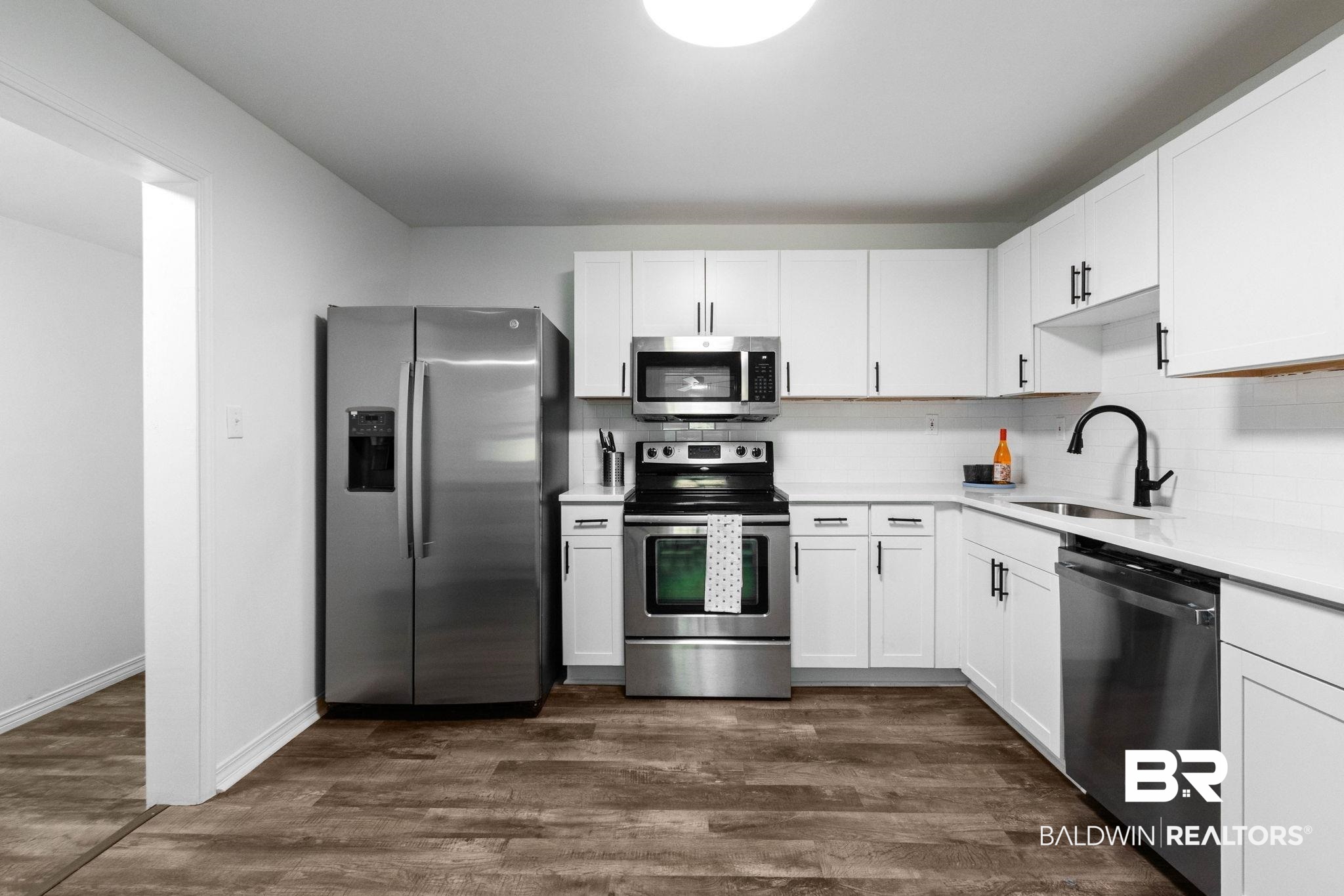 128 Bush Avenue Mobile, AL 36604 - Photo 9 of 40 Kitchen featuring stainless steel appliances, white cabinetry, dark wood-style floors, and backsplash