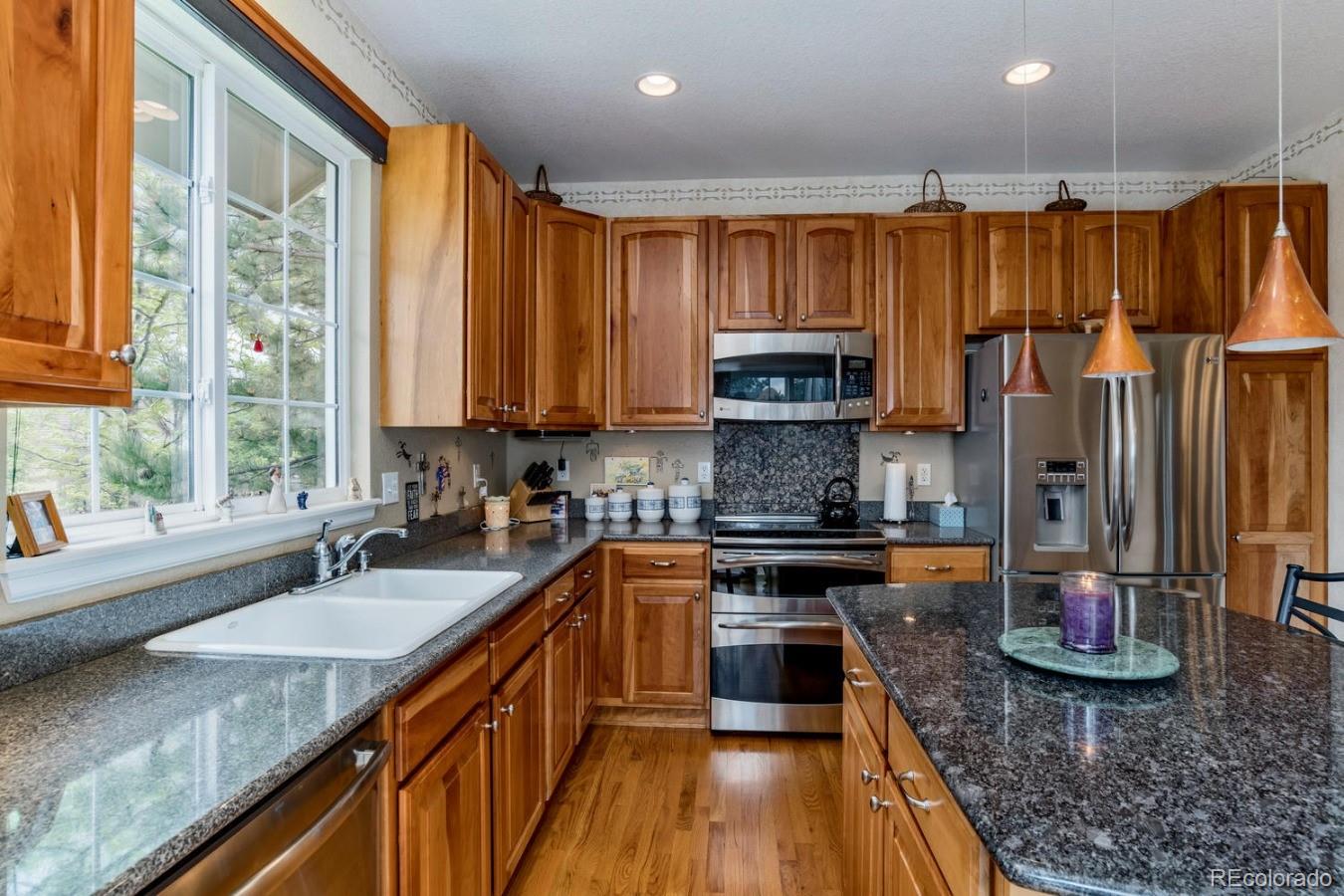 8974 Old Tom Morris Circle Highlands Ranch, CO 80129 - Photo 9 of 28 a kitchen with stainless steel appliances granite countertop a sink a stove and a wooden floors