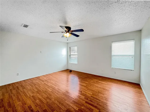an empty room with wooden floor fan and windows