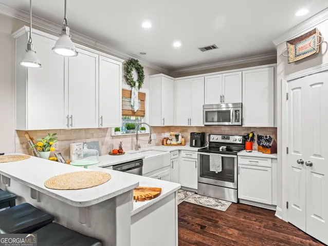 a kitchen with stainless steel appliances a stove a sink and white cabinets with wooden floor