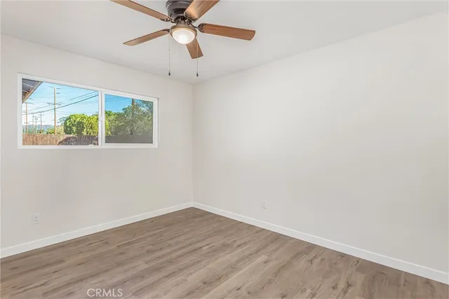 an empty room with wooden floor fan and windows