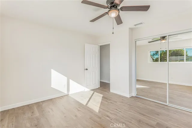 an empty room with wooden floor fan and windows