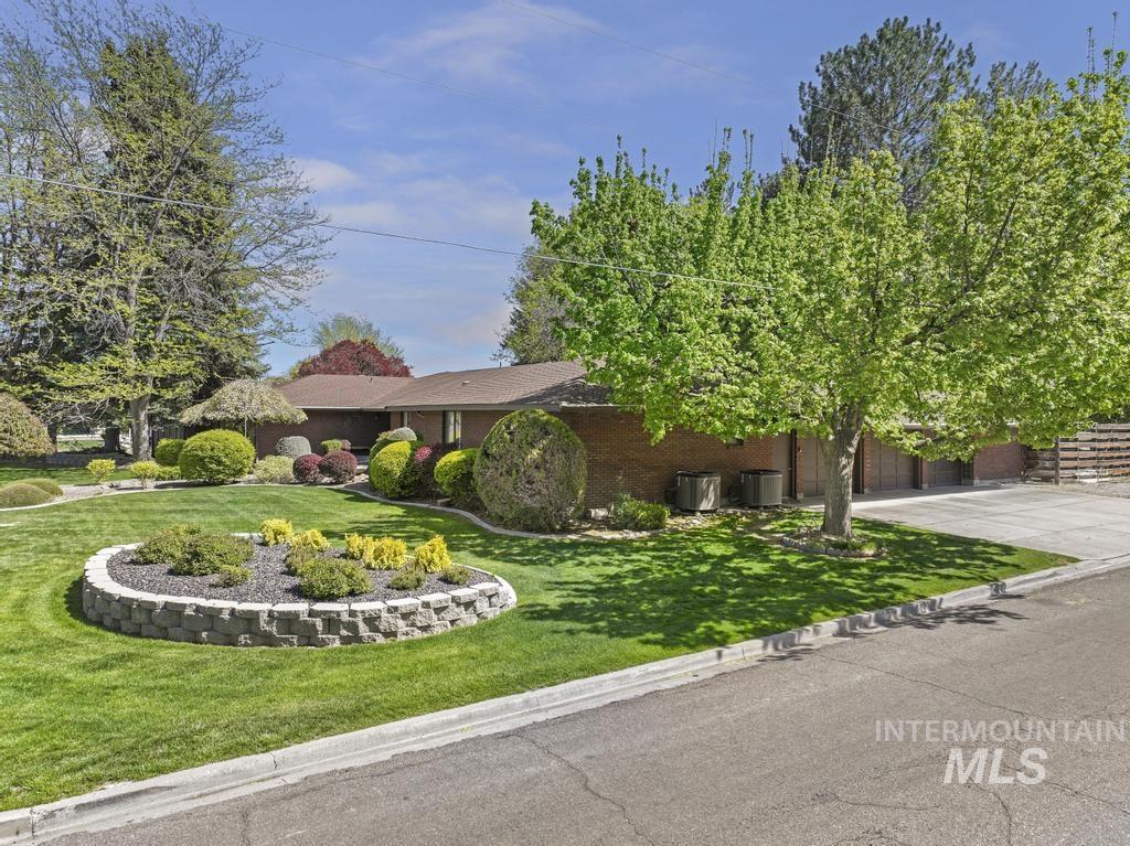 2018 Rancho Vista Drive Twin Falls, ID 83301 - Photo 49 of 50 Brick exterior property featuring a landscaped front yard with mature trees, a circular stone retaining wall garden bed, and a concrete driveway
