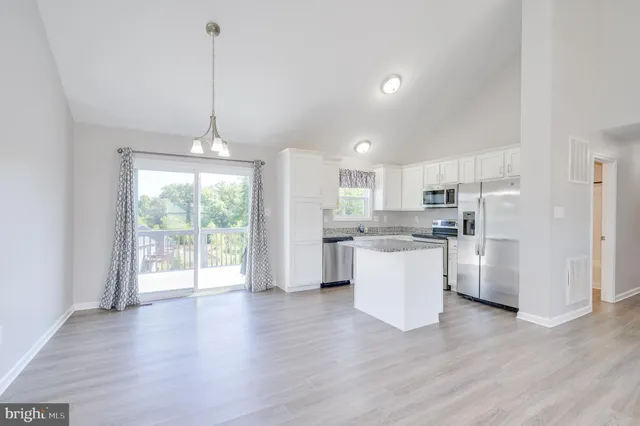 a kitchen with stainless steel appliances granite countertop a refrigerator a sink dishwasher a stove and white cabinets with wooden floor