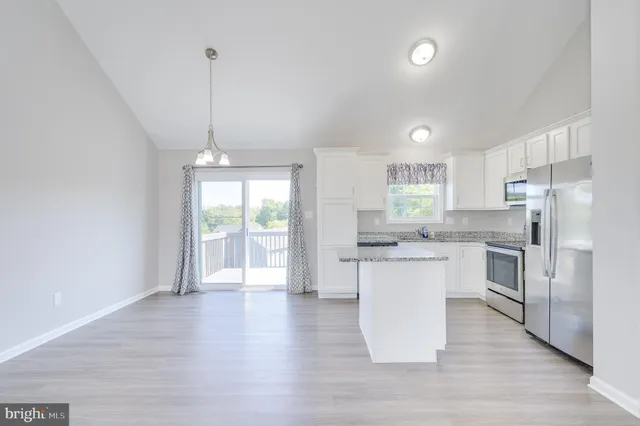 a kitchen with stainless steel appliances granite countertop a refrigerator a sink dishwasher a stove and white countertops with wooden floor