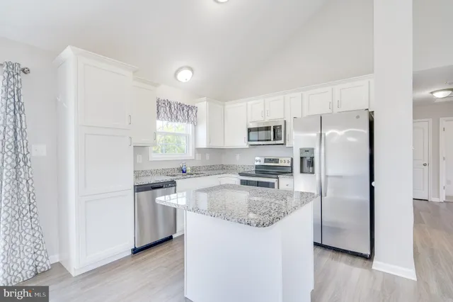 a kitchen with stainless steel appliances granite countertop a refrigerator a stove a sink a microwave a refrigerator and white cabinets with wooden floor