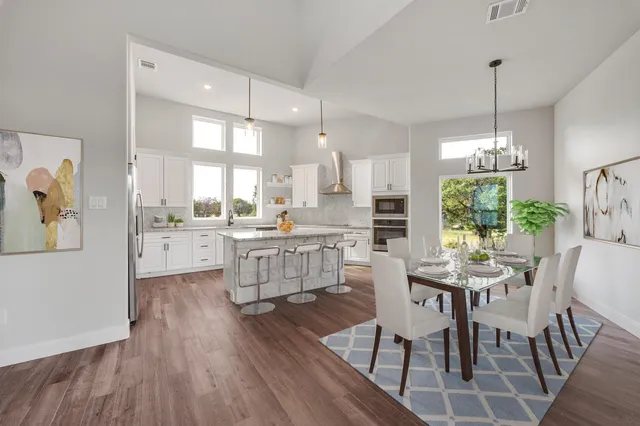 a kitchen with stainless steel appliances kitchen island granite countertop a stove a sink dishwasher a dining table and chairs with wooden floor