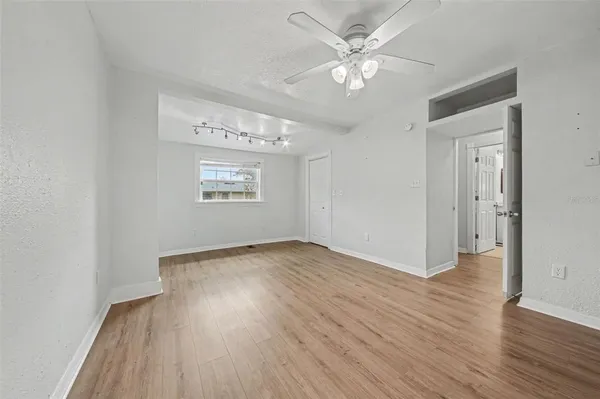 an empty room with wooden floor chandelier fan and windows