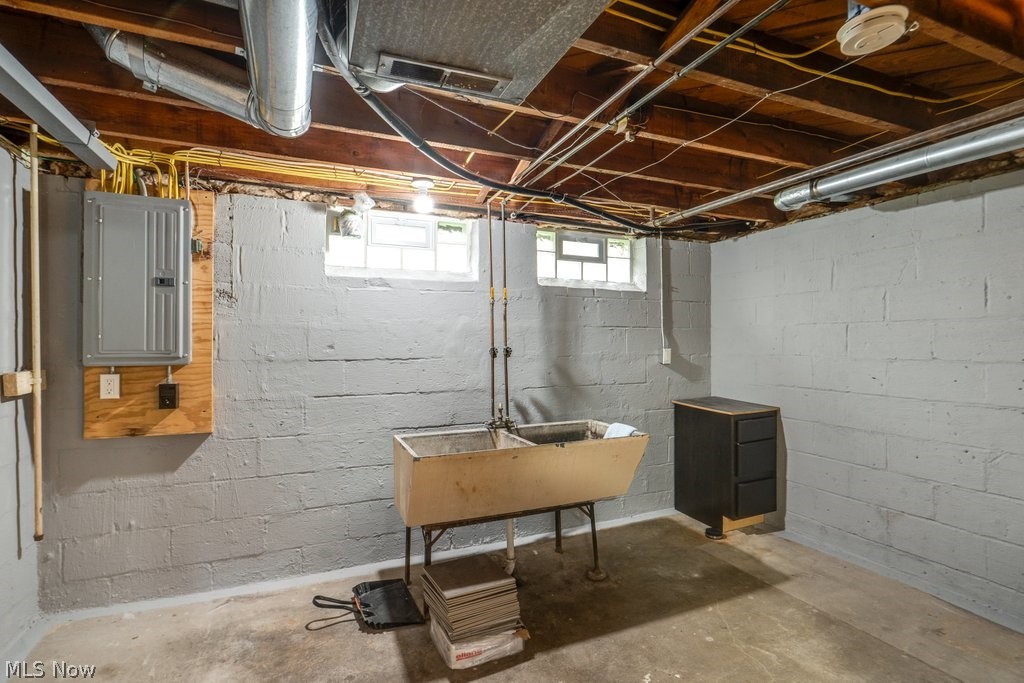 30000 Elgin Road Wickliffe, OH 44092 - Photo 25 of 30 Utility space featuring exposed ceiling joists, two glass block windows, a double basin utility sink, a wall-mounted electrical panel, and a standalone storage cabinet