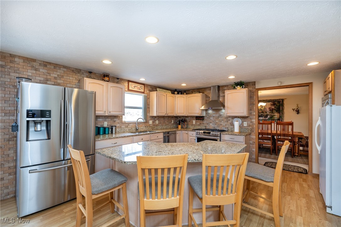 12181 Williams Road Homerville, OH 44235 - Photo 5 of 49 Kitchen with wall chimney range hood, appliances with stainless steel finishes, a center island, a kitchen breakfast bar, and light hardwood / wood-style floors