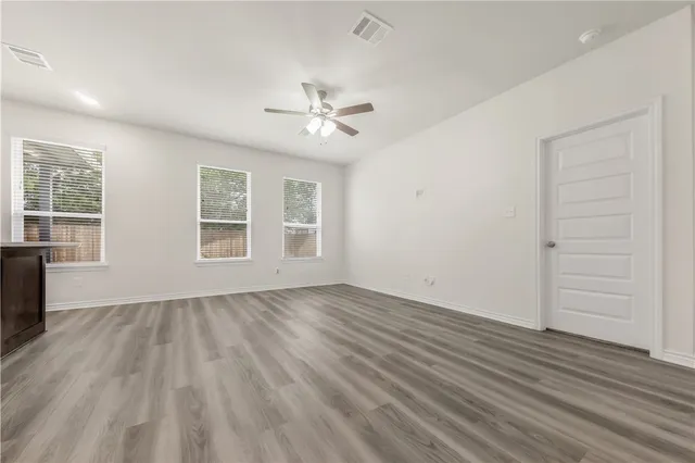 an empty room with wooden floor chandelier fan and windows