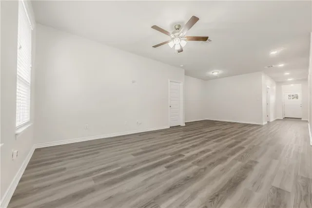 an empty room with wooden floor chandelier fan and windows