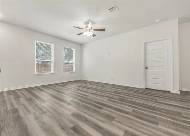 an empty room with wooden floor chandelier fan and windows