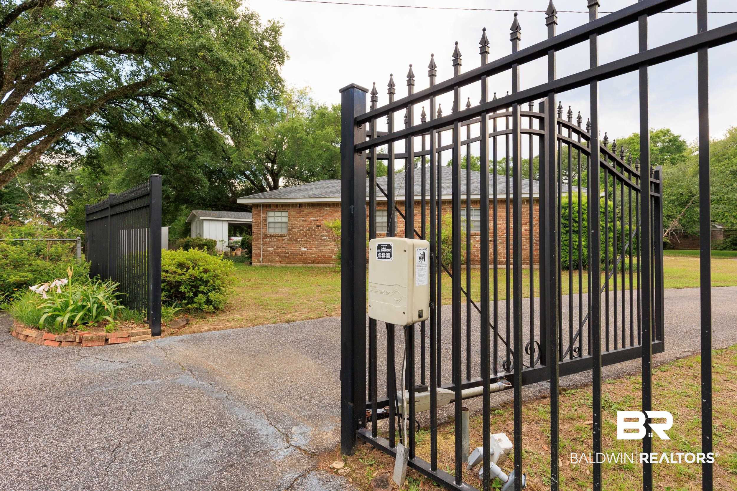 1367 Spring Valley Court Mobile, AL 36693 - Photo 24 of 29 Wrought iron gate entry with automatic opener, brick exterior residence, asphalt driveway, mature trees, and a garden shed
