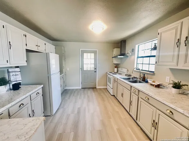 a large kitchen with granite countertop a refrigerator a sink dishwasher a stove and white countertops with wooden floor