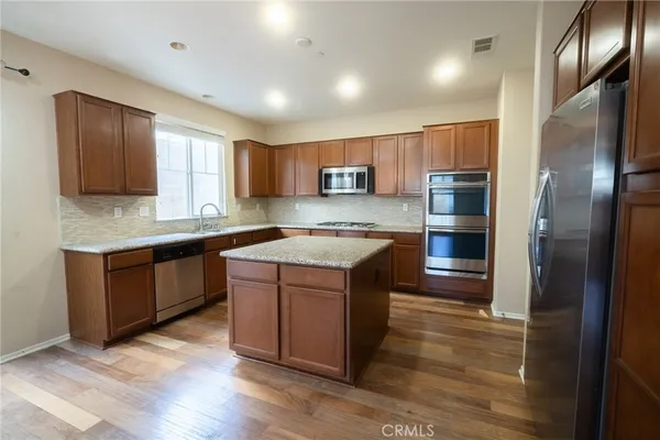 a kitchen with kitchen island granite countertop wooden floors stainless steel appliances a sink and a window