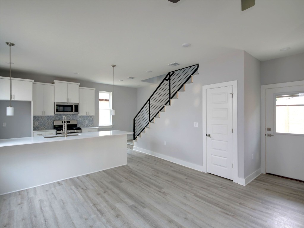 6111 Carnation Terrace, Unit 2 Austin, TX 78741 - Photo 7 of 34 Kitchen with white cabinetry, decorative light fixtures, appliances with stainless steel finishes, backsplash, and light wood finished floors