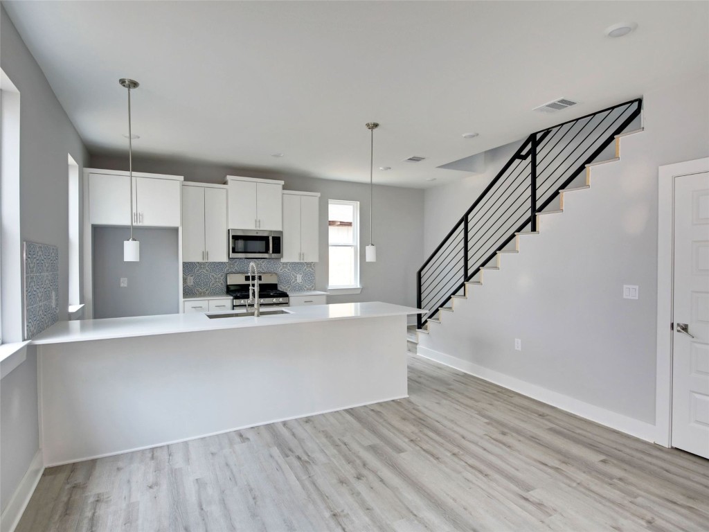 6111 Carnation Terrace, Unit 2 Austin, TX 78741 - Photo 9 of 34 Kitchen with white cabinetry, a peninsula, hanging light fixtures, stainless steel appliances, and light wood-style flooring