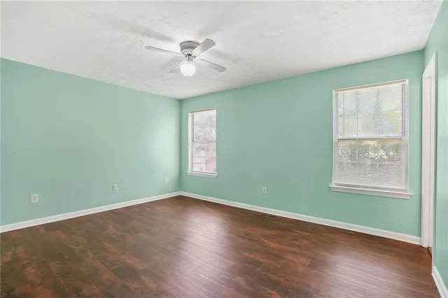 an empty room with wooden floor fan and windows