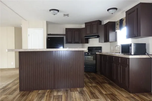 a kitchen with kitchen island granite countertop a stove top oven a sink and dishwasher a oven with wooden cabinets
