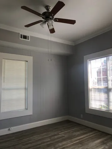 an empty room with wooden floor fan and windows