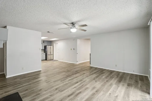 a view of an empty room with wooden floor and a ceiling fan