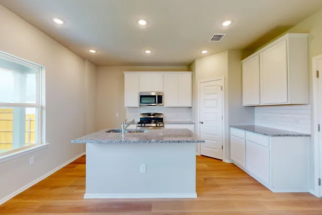 a large kitchen with stainless steel appliances granite countertop a stove a sink a refrigerator and white cabinets with wooden floor