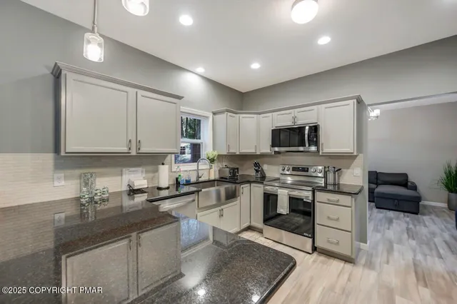 a kitchen with stainless steel appliances granite countertop a stove top oven a sink a refrigerator and white cabinets