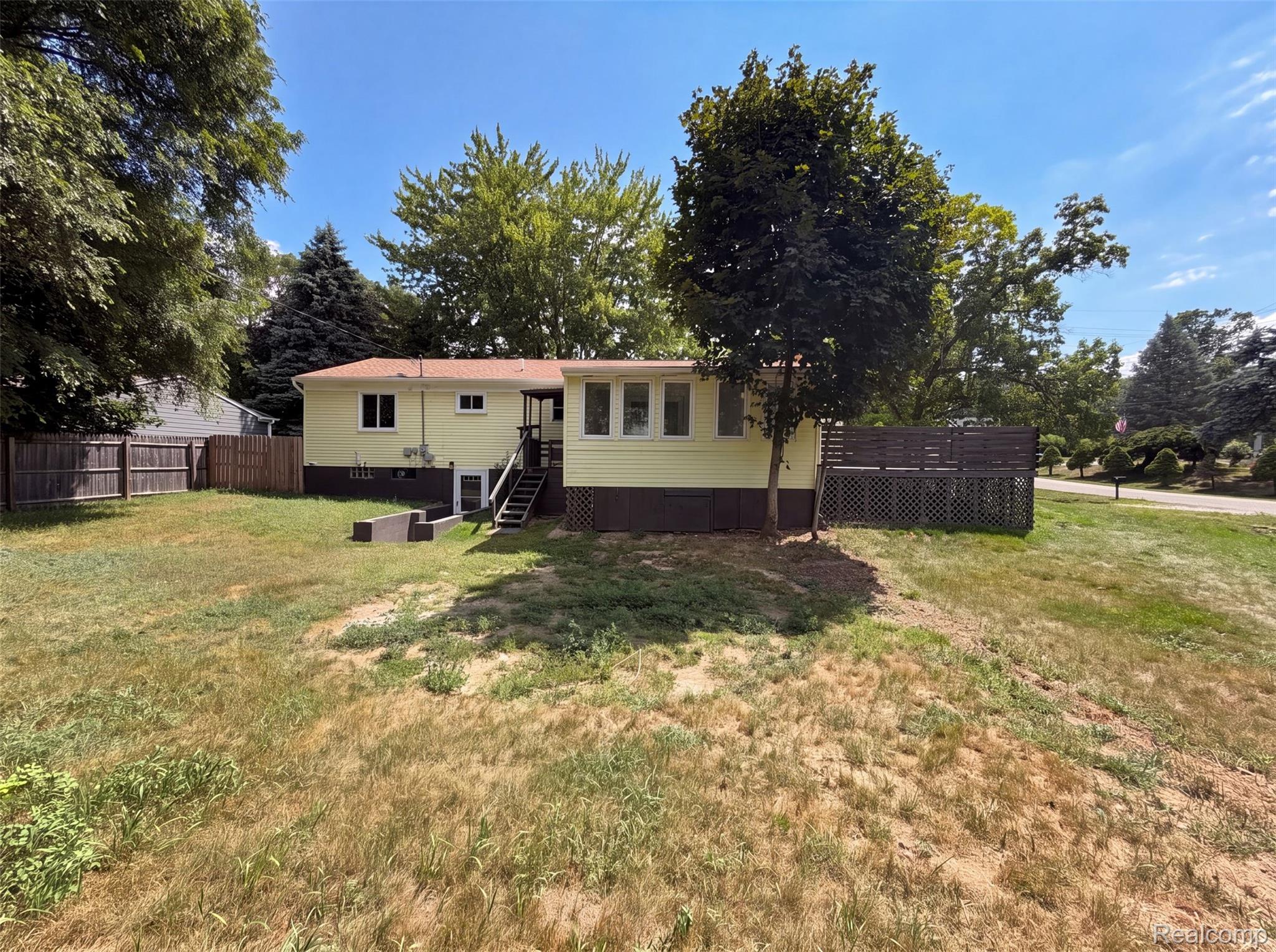 3211 24 Mile Road Utica, MI 48316 - Photo 18 of 18 Expansive yard space featuring a light-yellow exterior, a brown wood fence, and mature trees
