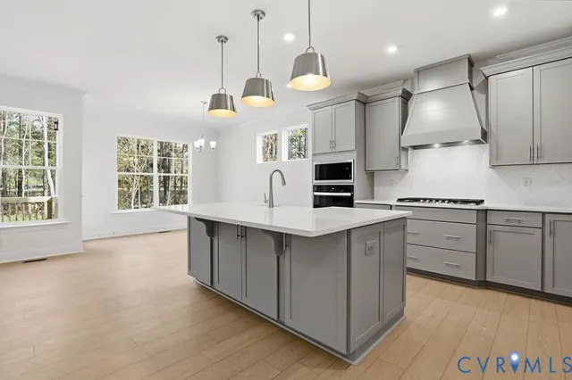 a large kitchen with stainless steel appliances a large counter top a stove a sink dishwasher a microwave oven and a dining table with wooden floor