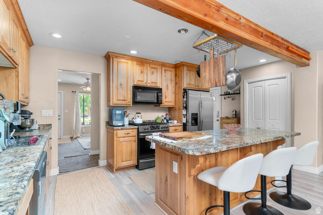 1489 North 400 West Bountiful, UT 84010 - Photo 9 of 47 Kitchen featuring warm wood cabinetry, granite countertops, stainless steel refrigerator, black range, and a central island with bar seating