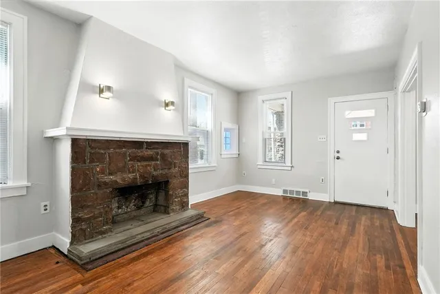 a view of an empty room with wooden floor fireplace and a window