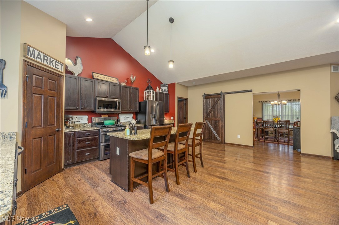 2851 Barnett Ridge Road Fleming, OH 45729 - Photo 16 of 40 Kitchen featuring appliances with stainless steel finishes, a barn door, high vaulted ceiling, a breakfast bar area, and wood finished floors