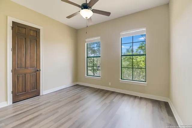 an empty room with wooden floor chandelier fan and windows