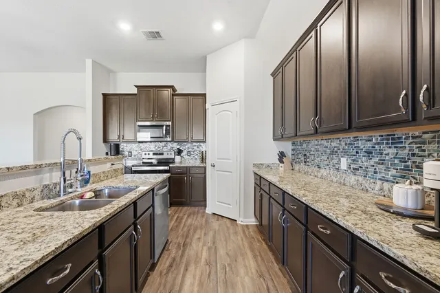 a kitchen with granite countertop stainless steel appliances a sink dishwasher stove refrigerator and cabinets with wooden floor
