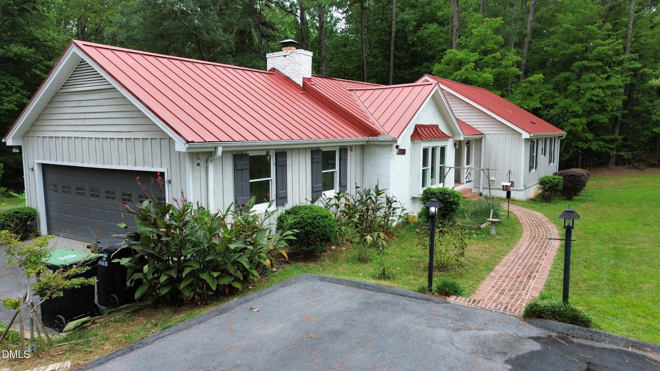 2329 Win Road Garner, NC 27529 - Photo 80 of 90 Red metal roof, white siding exterior, attached garage, brick-paved walkway, and exterior lighting fixtures