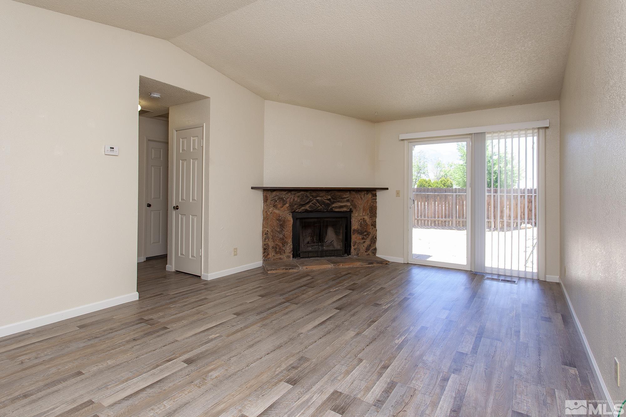 10046 Humite Lane Reno, NV 89506 - Photo 2 of 17 an empty room with wooden floor fireplace and windows