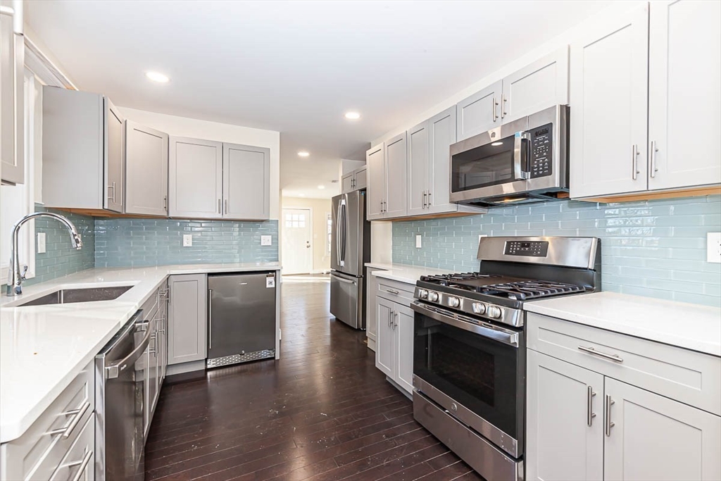 a kitchen with stainless steel appliances granite countertop a sink dishwasher a stove top oven a refrigerator with white cabinets and wooden floor