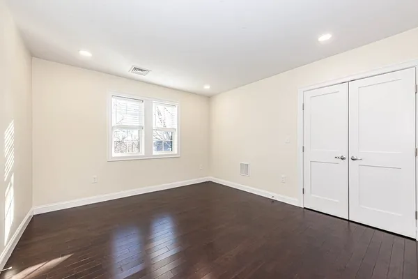 an empty room with wooden floor closet and windows