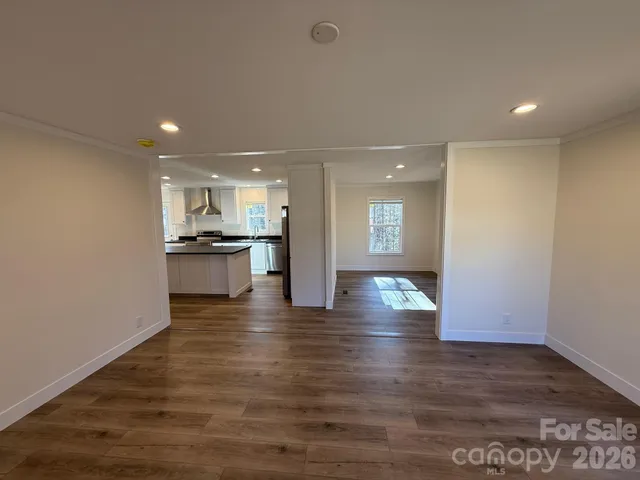 a view of an empty room and kitchen with wooden floor