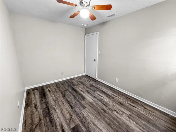 an empty room with wooden floor fan and windows