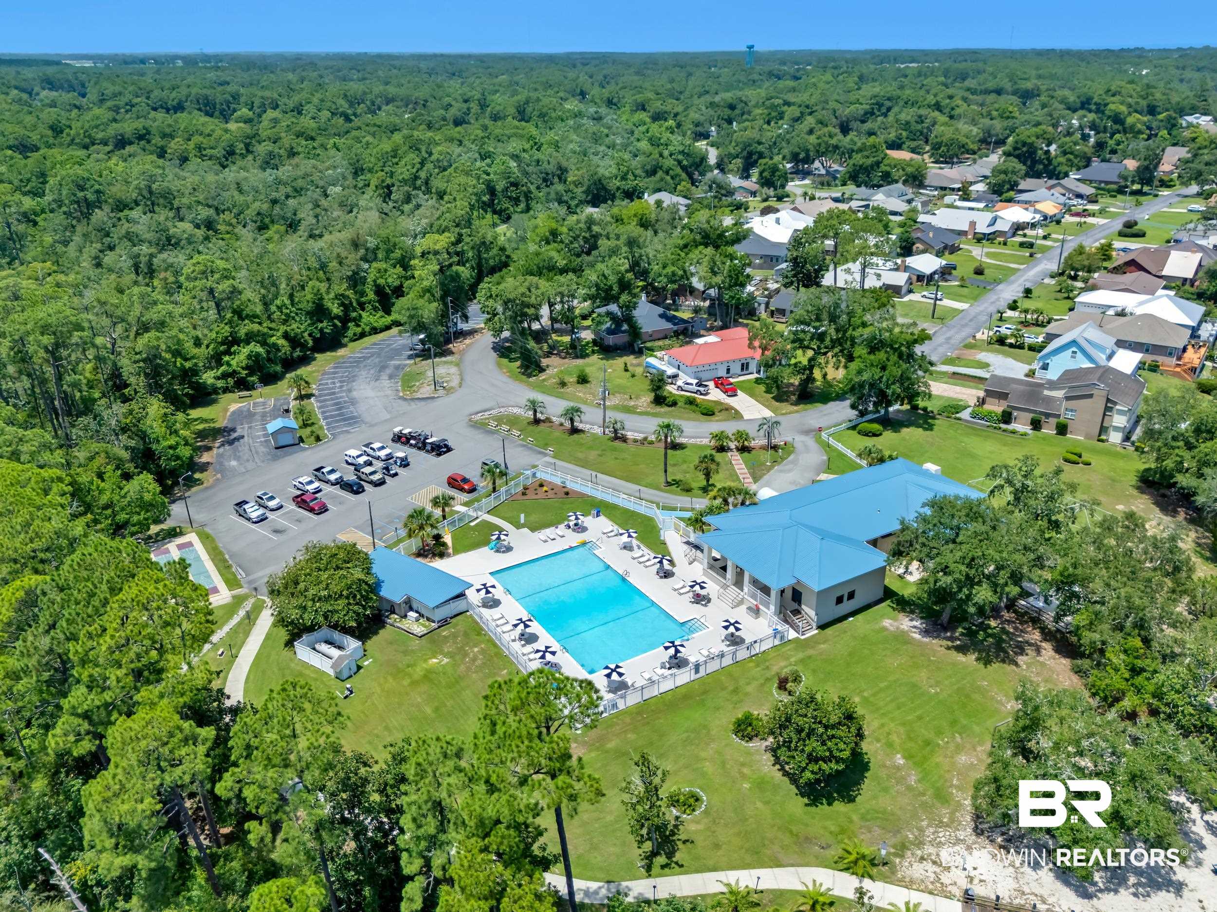 3070 Camino Real Loop Lillian, AL 36549 - Photo 45 of 46 Community amenities featuring a large outdoor swimming pool, a second smaller pool, a dedicated parking area, and a clubhouse with a bright blue roof, all surrounded by mature trees