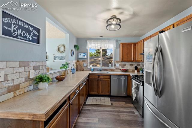 1830 Doherty Road Colorado Springs, CO 80916 - Photo 12 of 34 Kitchen featuring appliances with stainless steel finishes, dark hardwood / wood-style floors, tile countertops, backsplash, and sink